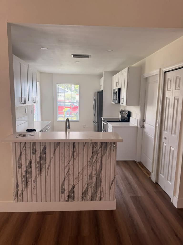 The same kitchen finished, with white cabinetry, a fluted marble peninsula and wood-look flooring