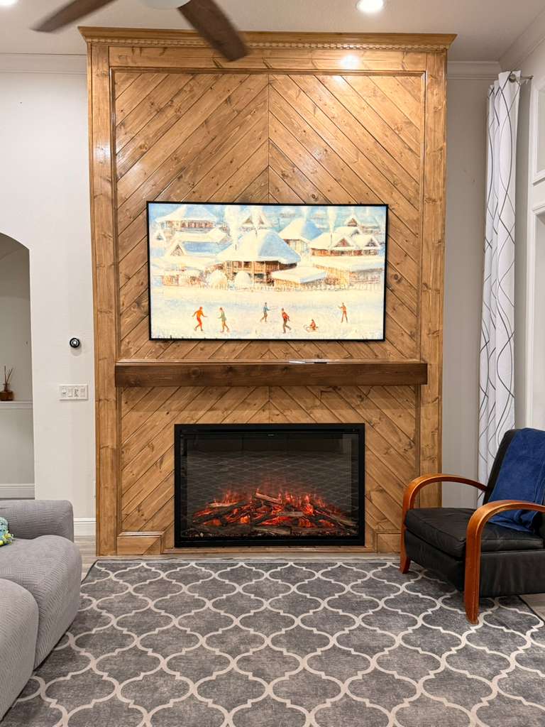 Custom chevron wood fireplace feature wall with a timber mantel and mounted television