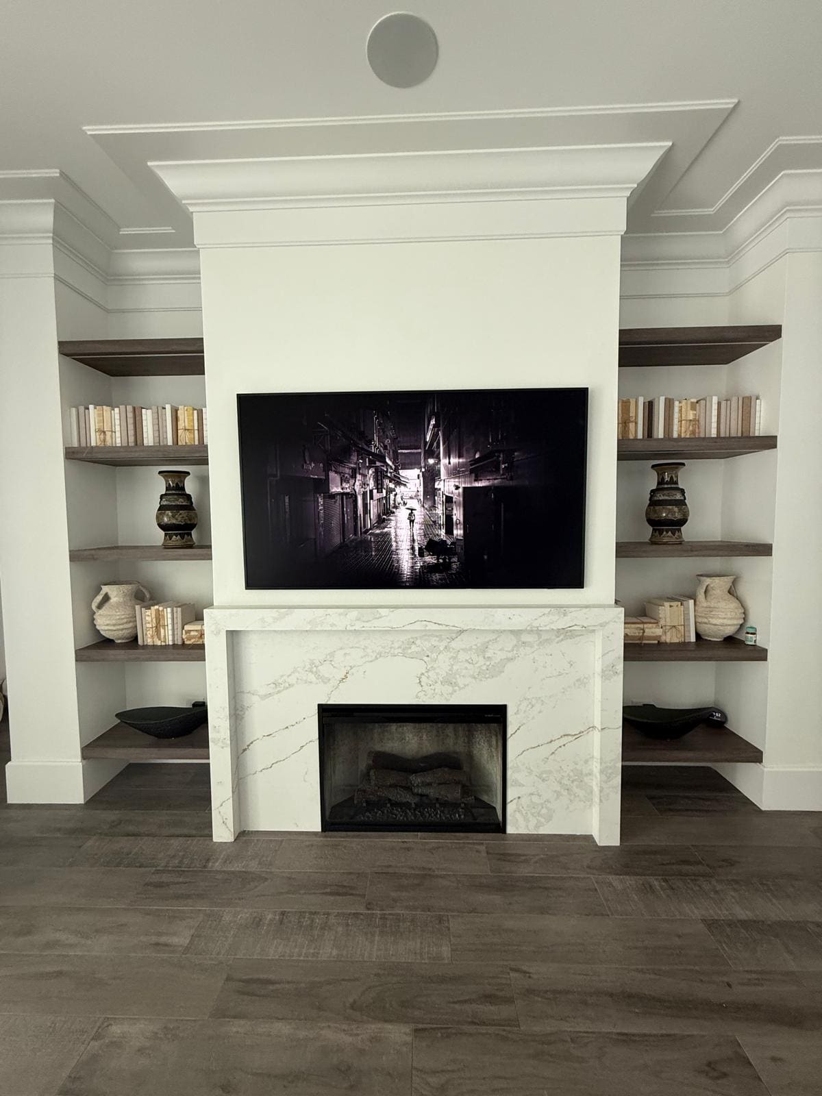 Custom fireplace with a quartz surround flanked by built-in floating shelves and crown moulding