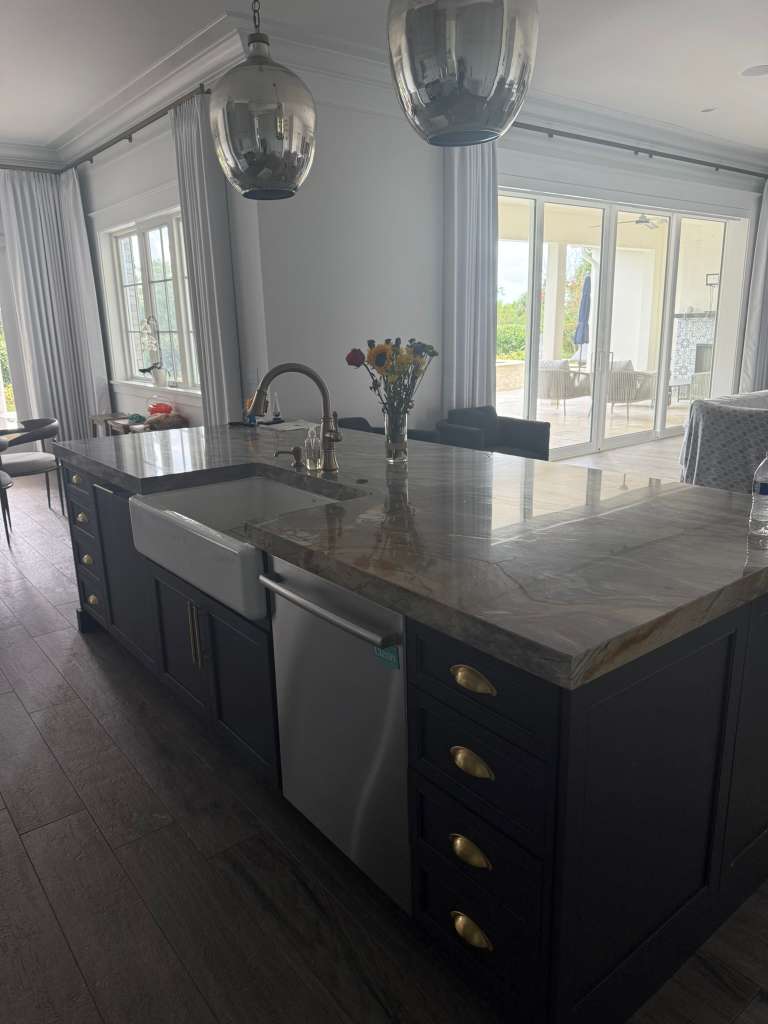 Kitchen island in navy cabinetry with a quartzite countertop, farmhouse sink and brass cup pulls