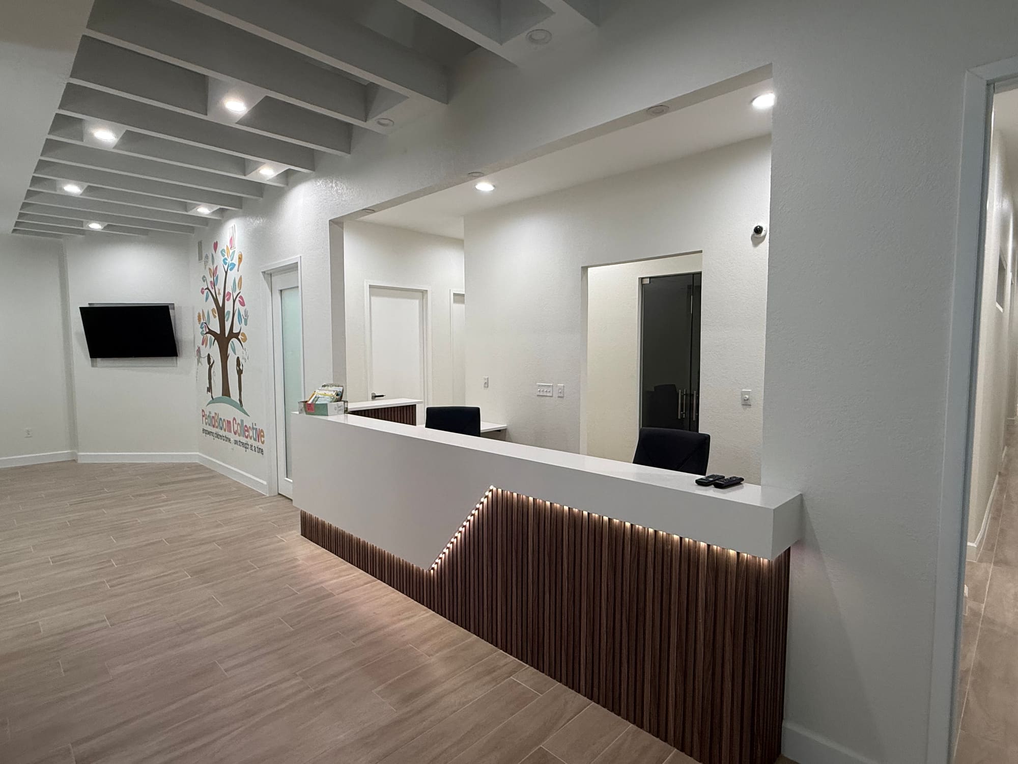 Remodeled office reception area with a backlit wood slat accent wall, custom reception desk and wood-look tile flooring