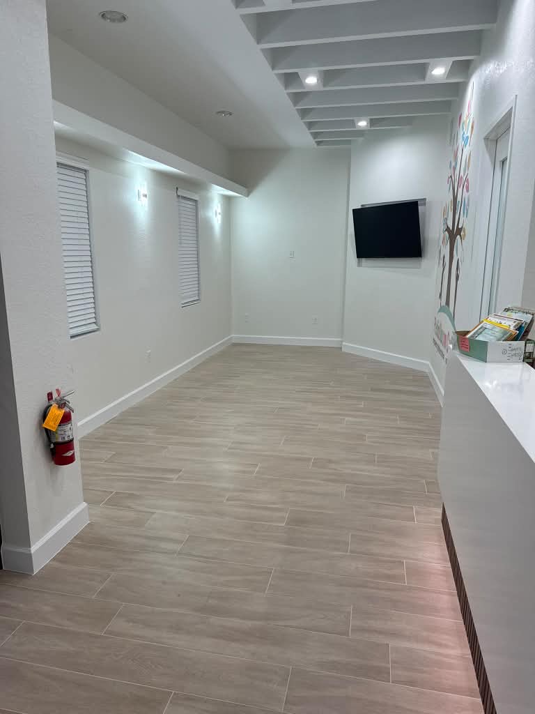 Office waiting area with wood-look tile flooring, a wall-mounted TV and a decorative wall mural