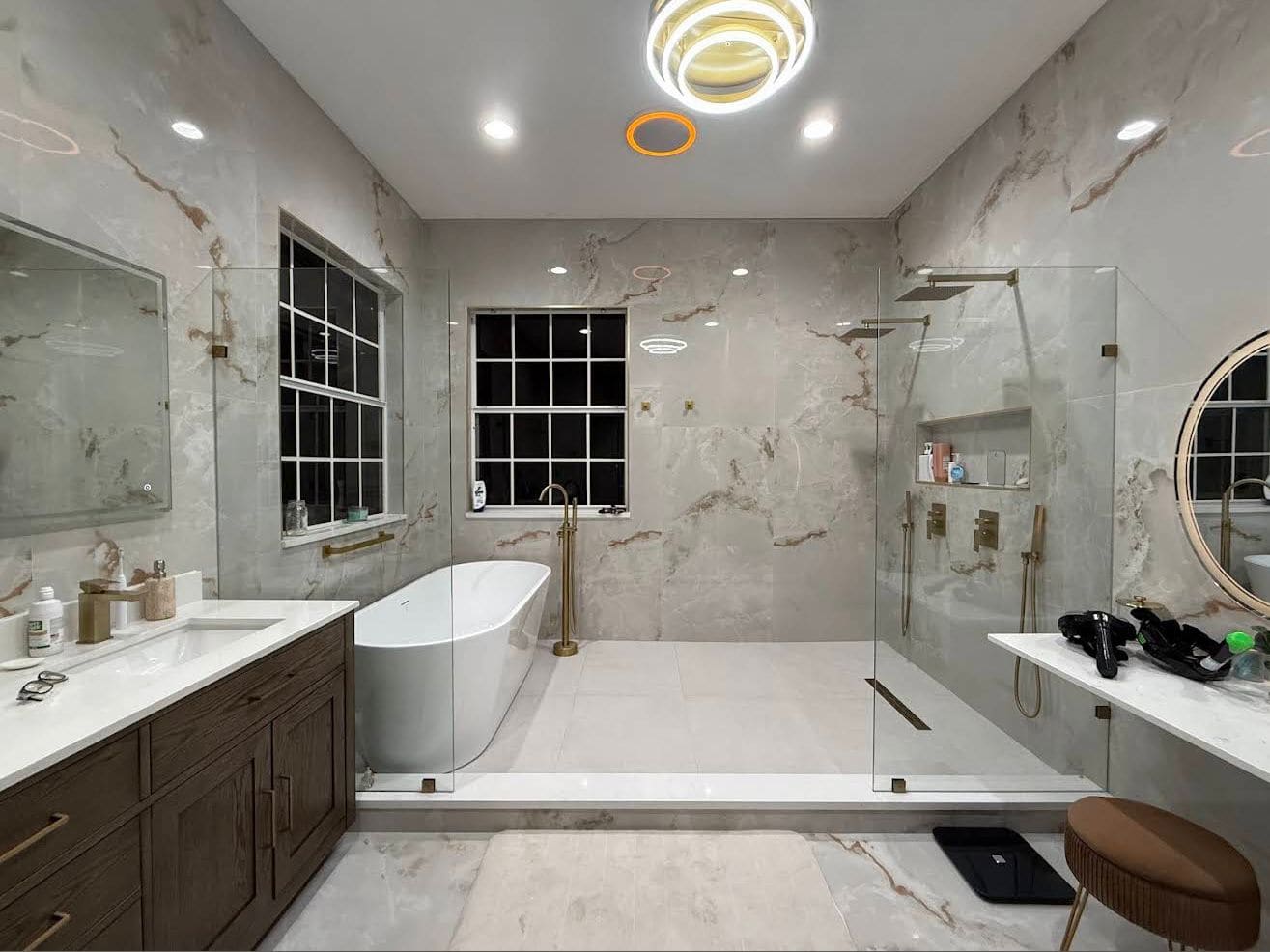 Primary bathroom remodel with a freestanding tub, curbless glass walk-in shower, marble-look tile and brass fixtures